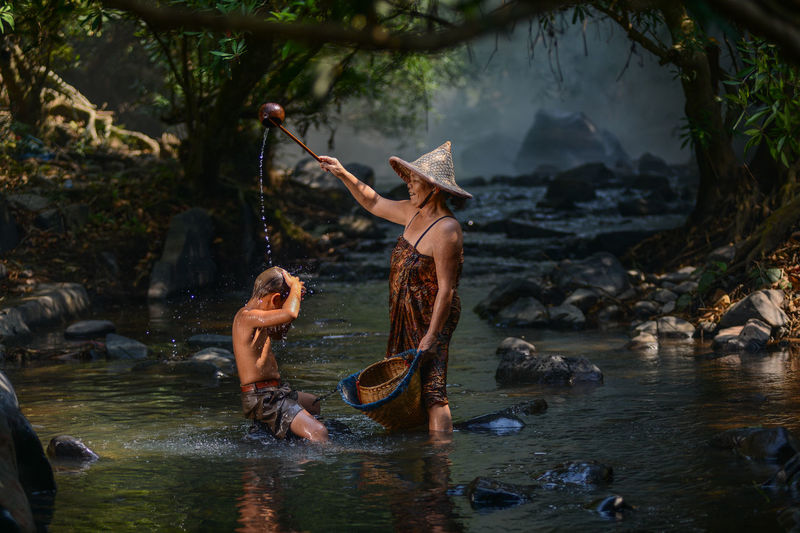 Side view of grandmother bathing grandson in river at forest