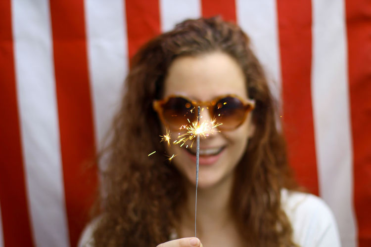  young redhead hispanic caucasian woman holding a sparkler standing in front of the american flag