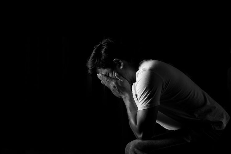 Side view of depressed man with head in hands against black background