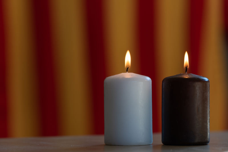 Close-up of illuminated candles on table against wall