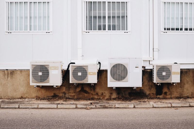 Air conditioners mounted on building by sidewalk