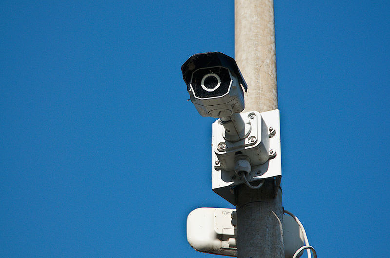 Low angle view of security camera at street against clear blue sky