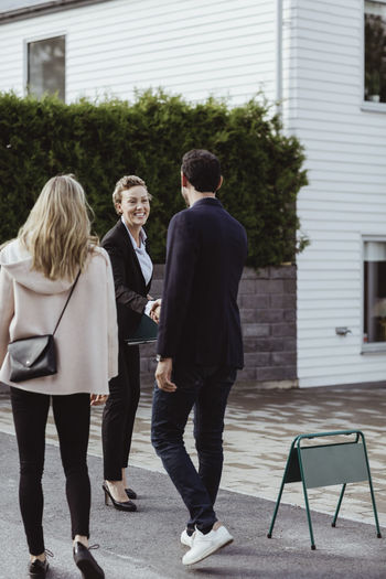 Smiling real estate professional greeting couple outside new house