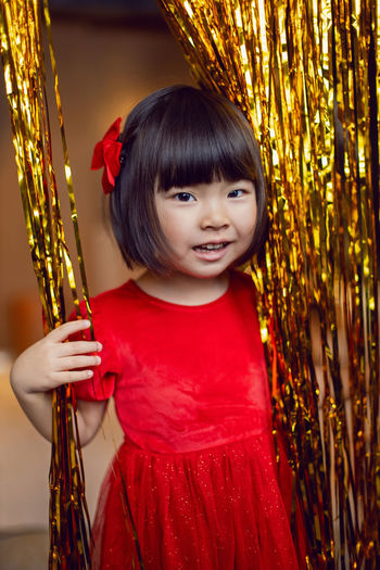 Portrait of a beautiful korean baby girl in a red dress at christmas with a gold decoration