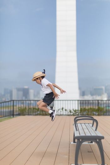 Side view of boy wearing hat while jumping on footpath against sky