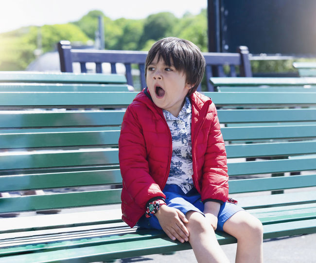 Boy yawning while sitting on bench