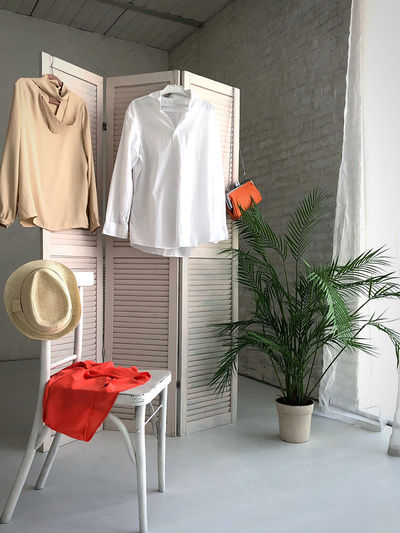 Fitting white room with window for women's clothing. straw hat, white shirt, blouse, orange handbag.
