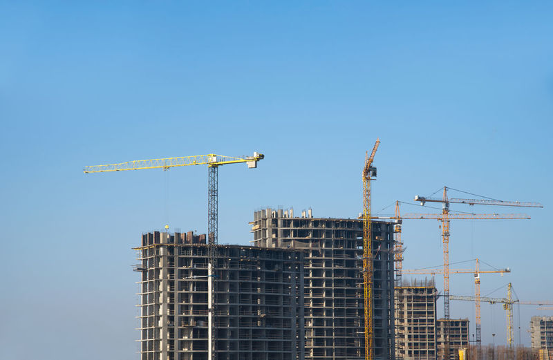 Low angle view of cranes on building against clear blue sky