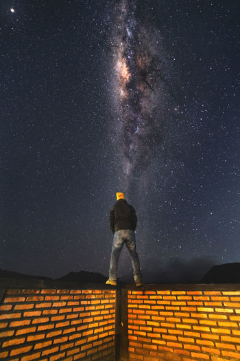 Rear view of man standing on brick wall against star field at night