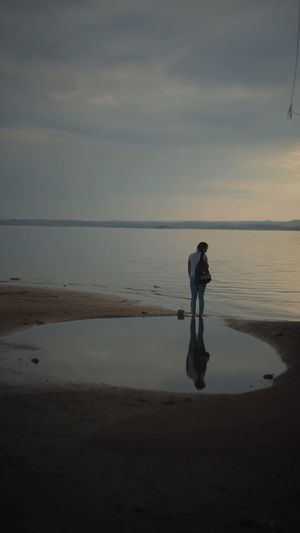 Woman standing on beach against sky during sunset