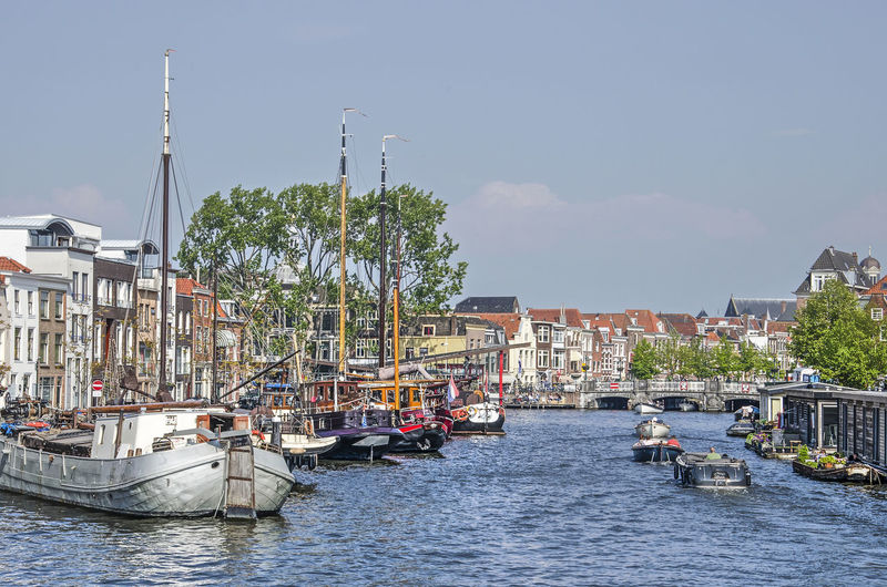 Sailboats in canal amidst buildings in city against sky