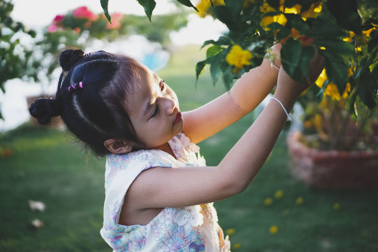 Side view of girl plucking flowers from plant at park