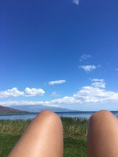 Low section of woman relaxing on blue sea against sky