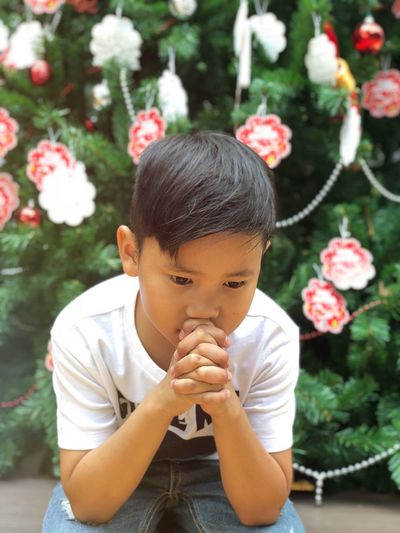 Thoughtful boy looking away while sitting against tree