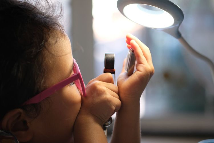Close-up of girl holding equipment by desk lamp 