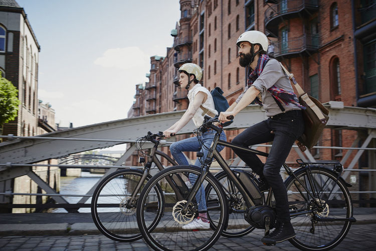 Germany, hamburg, couple riding electric bicycles at old warehouse district