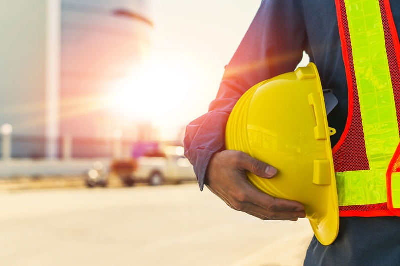 Midsection of man holding hardhat while standing outdoors