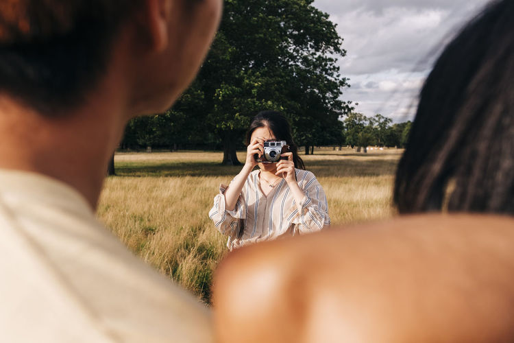 Woman photographing friends through camera at park