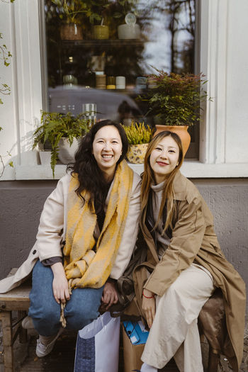 Portrait of happy female friends sitting together on bench