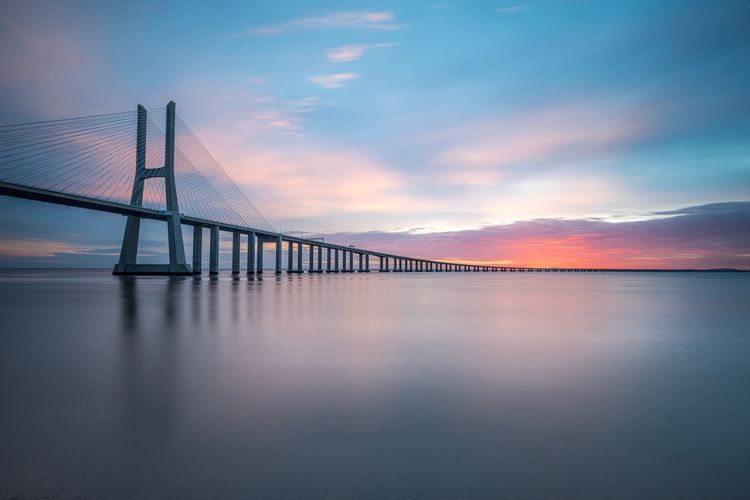 Vasco da gama bridge over tagus river against sky during sunset