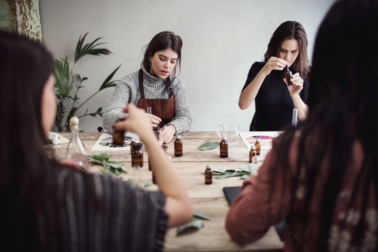 Multi-ethnic female colleagues preparing perfume while sitting at table in workshop