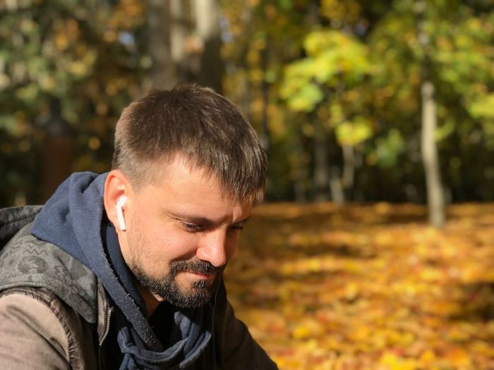 Bearded man listening music in park during autumn