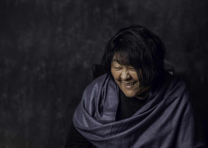 Laughing mature middle aged asian woman joyful cheerful.  female in early fifties, dark background