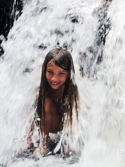 Smiling shirtless girl standing under waterfall