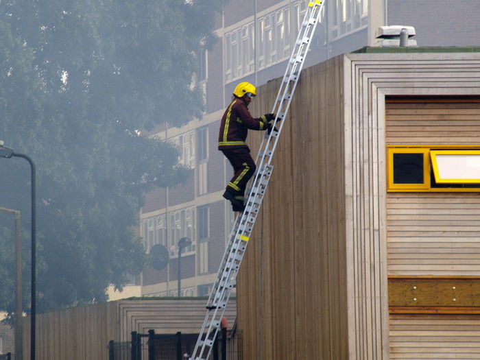 Side view of worker on ladder by building