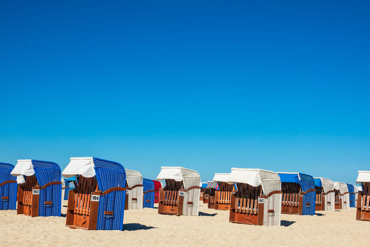 Hooded chairs at beach against clear blue sky during sunny day