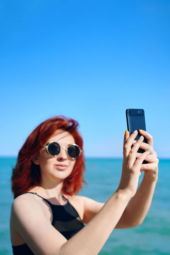 Portrait of young woman using mobile phone against blue sky