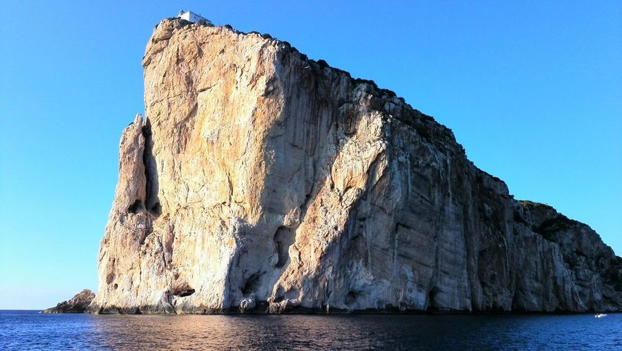 Rock formations in sea against clear blue sky