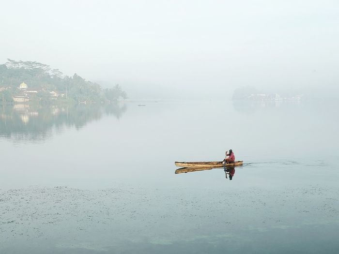 Man sitting in boat on lake against sky