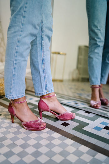 Unrecognizable female wearing jeans and open toe heels standing in front of mirror in modern apartment