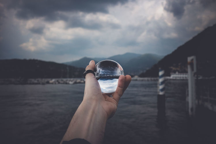 Cropped hand holding crystal ball against lake