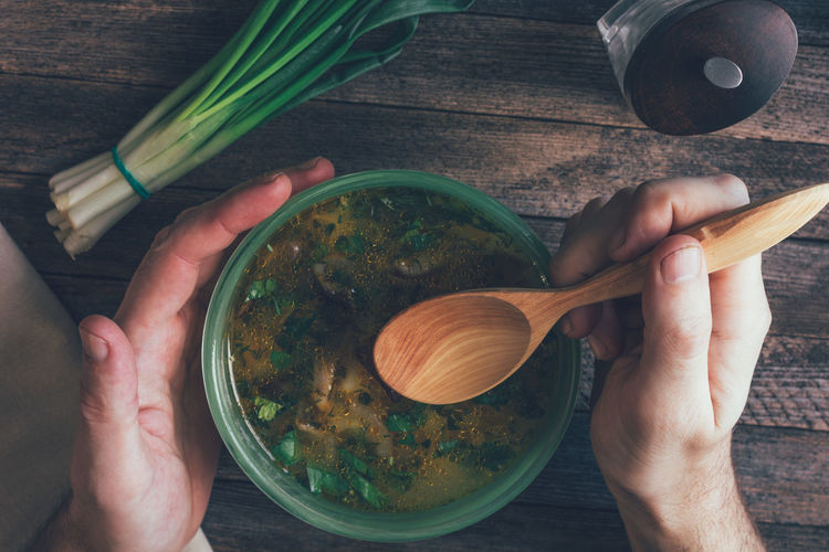 Man eats mushroom soup, green onions, pepper mill and a wooden spoon on old wooden table