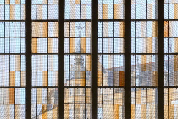 Through a large window with rectangular fragments, one can see the yellow facades of an old city