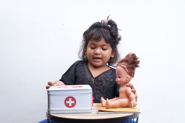 Girl with first aid kit playing with doll over white background