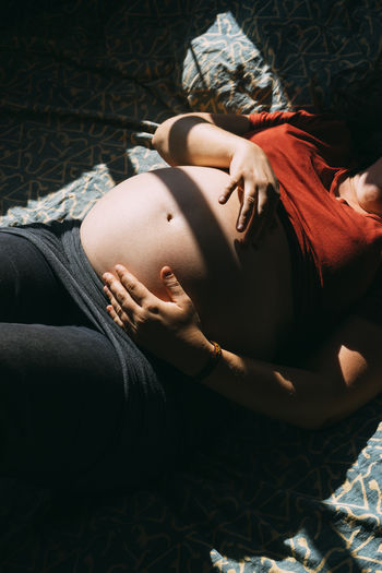 Midsection of pregnant woman lying down on bed at home