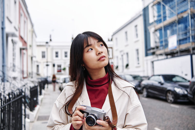 Thoughtful woman holding camera in city