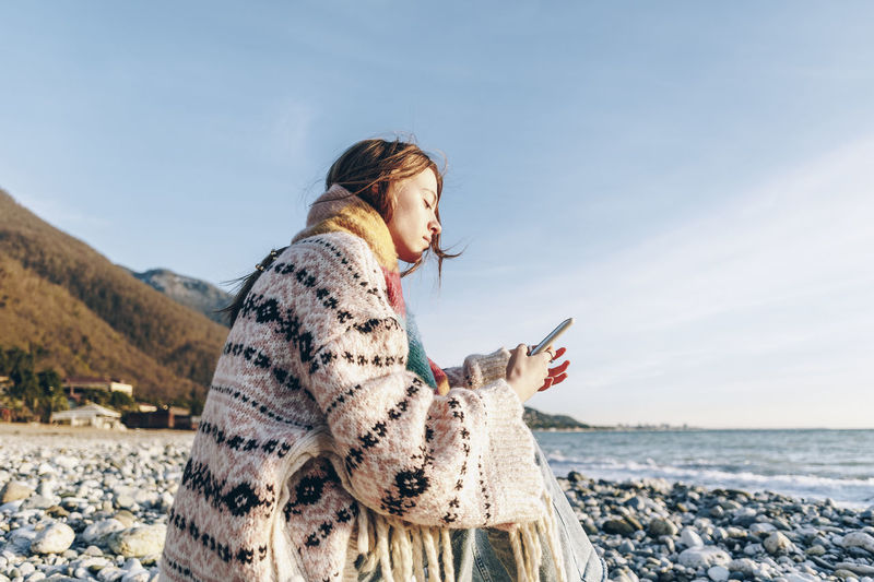 Teenage girl using smart phone while sitting at beach, gagra, abkhazia