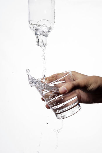 Close-up of hand pouring water from glass against white background