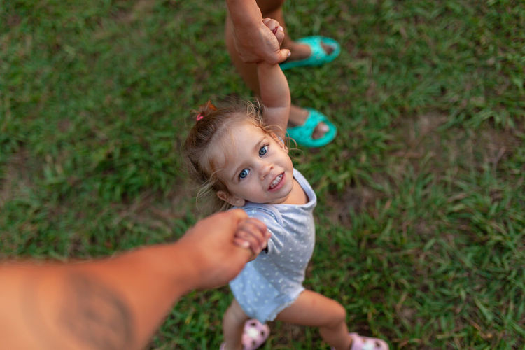 Portrait of cute girl holding parents hand on field