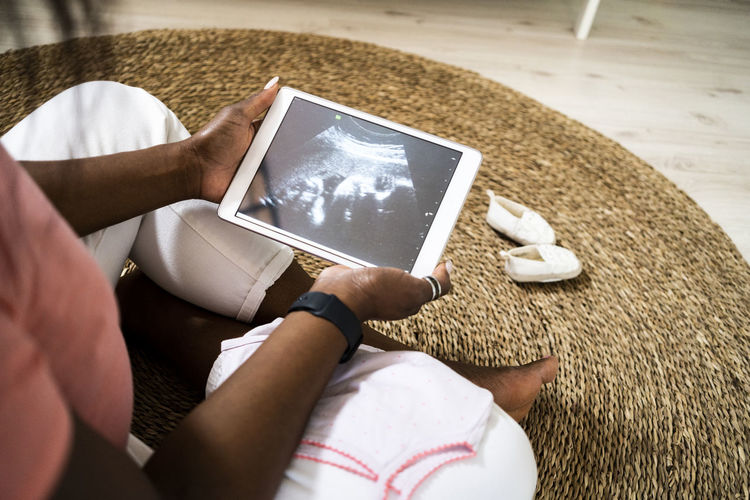 Pregnant woman holding digital tablet with ultrasound video at home