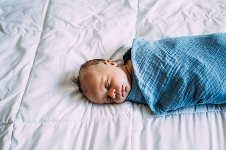Overhead of newborn baby napping on white blanket