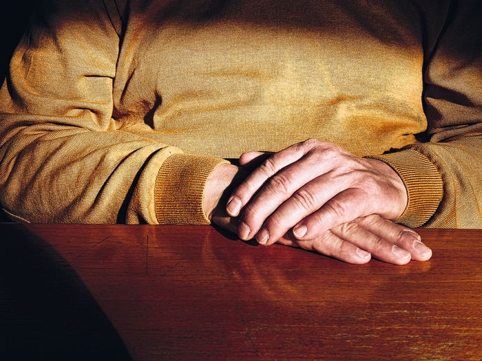 Midsection of man with hands clasped sitting at table