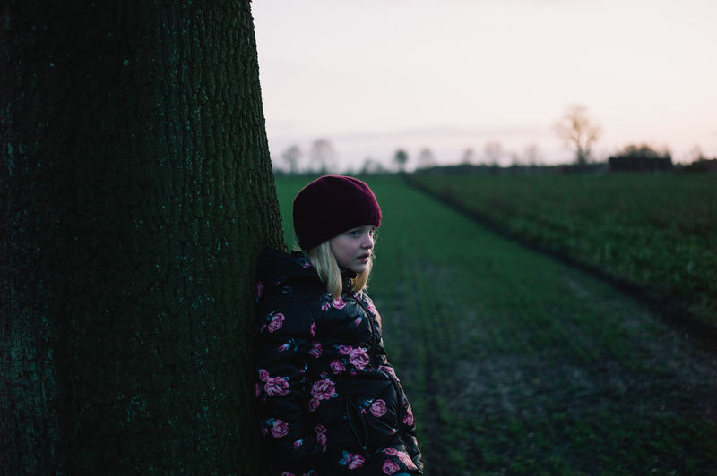 Girl standing by tree on field against sky