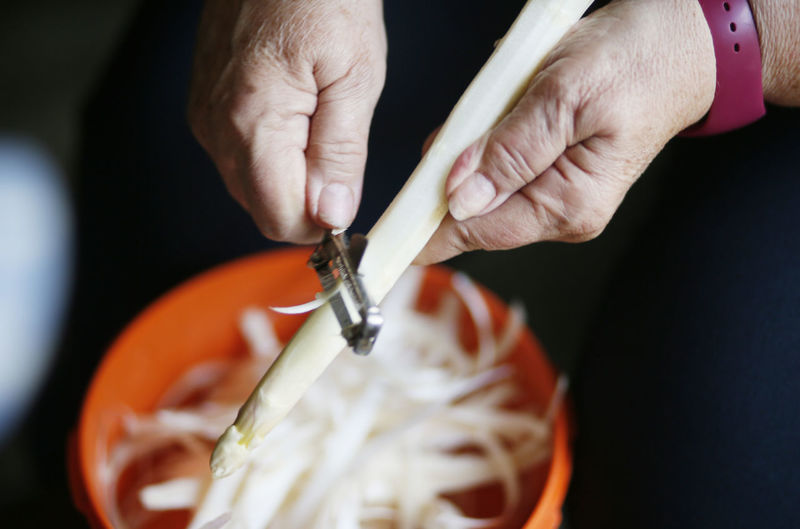 Cropped hands of woman peeling off asparagus in kitchen