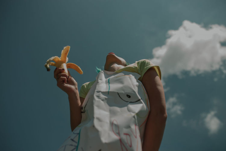 Low angle view of woman holding banana against sky