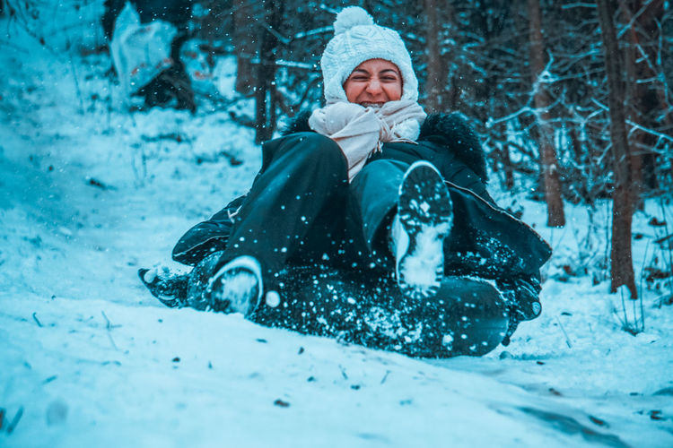 Full length of woman sitting on snow covered tree during winter